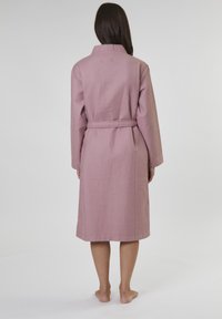 Bata de baño de textura de gofre rosa, con cuello, mangas largas y cinturón en la cintura. Diseño hasta la rodilla, acabado liso y sin patrones visibles.