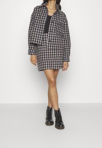 Ensemble jupe et veste en mélange de laine écossais bleu marine et beige. Présente une coupe décontractée, des poches avant et est assortie à des bottes noires à lacets.