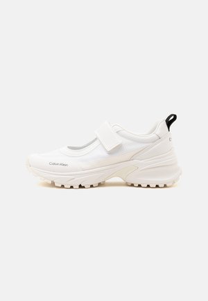 Scarpa sportiva bianca Calvin Klein con suola spessa e cinturino in velcro, design basso e linguetta nera sul tallone.
