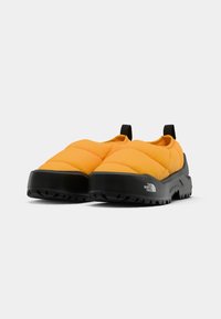 Chaussures slip-on rembourrées de couleur jaune vif avec un design matelassé, semelle en caoutchouc noir et languettes au talon pour faciliter l'enfilage.
