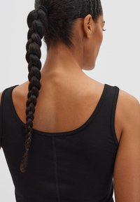 Zwart tanktop met een uitgeholde rug, gemaakt van zacht, rekbaar materiaal. Voorzien van nette stiksels en een smal schouderbandje met een gevlochten paardenstaart.