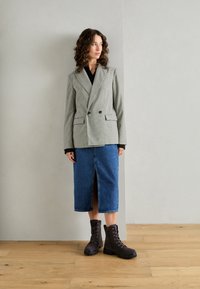 Blazer doppiopetto grigio e nero a scacchi, abbinato a una gonna in denim blu di lunghezza media con uno spacco frontale e stivali neri con lacci.