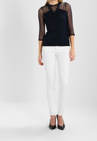 Granatowa bluzka z przezroczystymi, trzech ćwiartkowych rękawkami, pokryta wzorem kropek. Zestawiona z białymi, dopasowanymi dżinsami i czarnymi szpilkami.