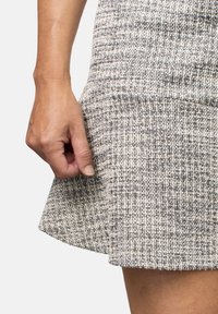 Falda texturizada y estampada en gris y crema con dobladillo acampanado. Mano cerrada a un lado. El material parece tejido y estructurado.