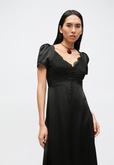 Zwarte satijnen jurk met kanten lijfje, pofmouwen en een voorzijde met knopen. De halslijn is gegolfd, benadrukt door kantdetails.