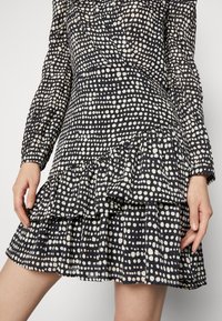 Vestido negro con lunares blancos, mangas largas, dobladillo con volantes y tejido texturizado, con una cintura ajustada y un diseño de falda fluida.