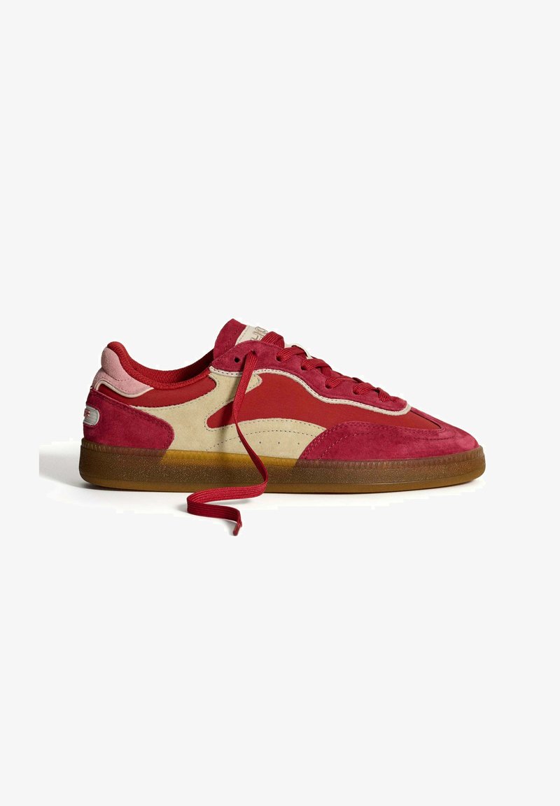 Zapatillas de ante rojas y beige con una suela de goma, que presentan cordones rojos, cortes laterales y un diseño de upper texturizado.