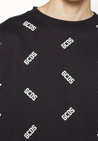 Sudadera negra con un patrón repetido del logo en blanco "GCDS", textura suave y diseño de cuello redondo.