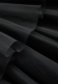 Couches de tissu noir transparent avec une texture fine en maille, pliées et superposées pour créer des ombres douces et de la profondeur.