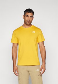 Gelbes Crewneck-T-Shirt aus weichem Material, mit einem kleinen weißen Logo auf der linken Brust. Kurzarm und im regulären Schnitt.