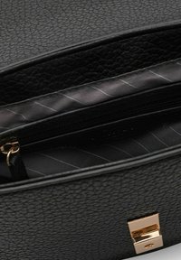 Interior de bolso de cuero negro texturizado con un bolsillo con cremallera y forro de tela a rayas; cuenta con un cierre de clasp tono dorado.