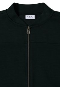 Svart zip-up jacka med hög krage, tillverkad av ett mjukt material. Har en metallblixtlås och en logotyp sydd i kragen.