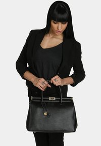 Bolso de mano de piel negra con una forma estructurada, asas superiores, herrajes metálicos y un detalle de candado. Acabado texturizado y acentos pulidos.