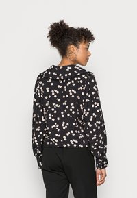 Blusa com estampado floral em fundo preto, mangas longas e gola. Apresenta um corte folgado com detalhes franzidos nos ombros.