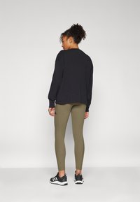 Μαύρη ριπ χοντρή μπλούζα συνδυασμένη με ελαιόπρασινα εφαρμοστά κολάν, συμπληρωμένη από μαύρα αθλητικά παπούτσια με λευκές λεπτομέρειες.