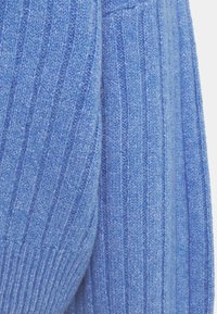 Tissu de pull bleu en tricot avec un motif de côtes verticales. Texture douce, épaisseur moyenne et léger brillant, mettant en valeur le détail du tricot.