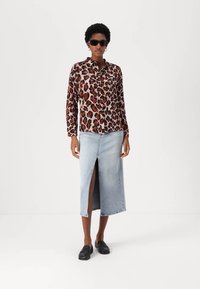Leopard print button-up shirt in shades of brown and beige, paired with a light blue denim skirt featuring a front slit. Black loafers complete the look.