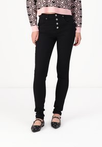 Schwarze hochtaillierte Jeans mit fünf Knöpfen, schmaler Schnitt, aus Baumwollmischung, kombiniert mit einem pinkfarbenen, herzgemusterten Cropped-Pullover und schwarzen Ballerinas.