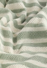Manta de punto con rayas alternas en verde y crema. La textura varía entre patrones de punto sólido y abierto. Material suave y ligero.