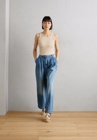 Top in beige abbinato a jeans a vita alta, larghi, di colore blu chiaro e sandali con zeppa in legno. Ambientato su uno sfondo neutro.
