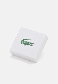 Hvit teksturert rektangulær boks med en grønn krokodille-logo på forsiden, med skarpe kanter og en glatt overflate.