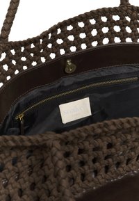 Sac fourre-tout tissé marron avec garniture en cuir, doublure intérieure noire, poche à fermeture éclair dorée et étiquette blanche portant l'inscription "soaked studio".