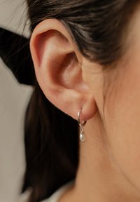 Boucle d'oreille en argent avec une petite perle pendante. Le design présente une texture lisse et une forme simple et élégante.
