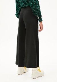 Zwarte wijde broek gemaakt van een zacht materiaal, met een hoge taille en een gladde textuur, gecombineerd met witte sneakers en gele veters.