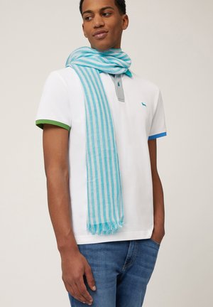 Écharpe rayée bleu clair et blanche drapée autour du cou, faite d'un tissu léger. Associée à un polo blanc et un jean bleu.