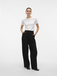 Top bianco a maniche corte con scollo a barca, abbinato a pantaloni larghi neri a vita alta e scarpe piatte marroni. Orecchini semplici completano l'outfit.