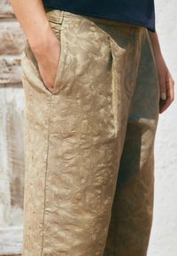 Helle beigefarbene, floral gemusterte Hose mit strukturiertem Finish. Verfügt über Seitentaschen und einen lockeren Schnitt.