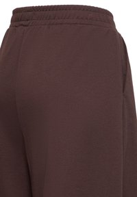 Pantalon marron foncé avec ceinture élastique et poches latérales, présenté en gros plan de dos et de côté.
