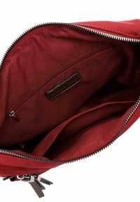 Sarkanas auduma somas iekšpuse ar rāvējslēdzēju, kurai ir ādas etiķete un divas iekšējās kabatas, gluda tekstūra un metāla rāvējslēdzēja aizdare.