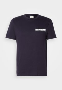 Tamsiai mėlynas medvilninis marškinėliai su apvalia iškirpte, trumpomis rankovėmis ir balta Calvin Klein logotipu, atspaustu kairėje krūtinės pusėje.