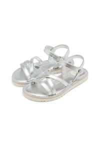 Sandali metallici argento con fasce incrociate e suola piatta bianca. Il materiale superiore è lucido e il design presenta fibbie regolabili.