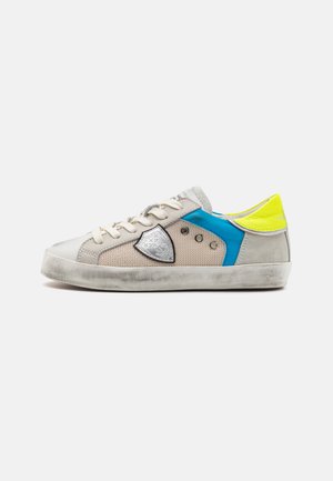Beige sneaker with mesh and suede material, featuring blue and neon yellow accents, silver hardware detail, and a textured rubber sole.