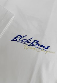 Witte katoenen t-shirt met blauwe en gele geborduurde tekst, waaronder "Blick Bums" en "Daytona Race Champions 1967."