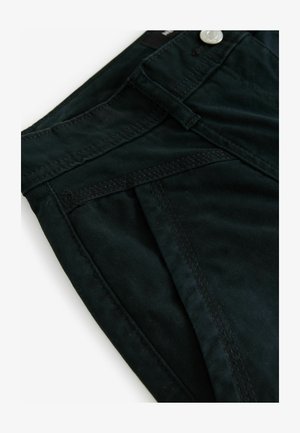 Tamsiai žalia medvilnė su lygiu paviršiumi, pasižyminti siūtomis siūlėmis ir sidabro mygtuku, esančiu šalia juosmens.