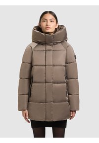 Puffer jacket in taupe with a high, lined collar. Features quilted design, side pockets, and a relaxed fit, suitable for cold weather.