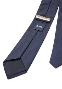 Gravata azul-marinho com textura estriada, apresentando um rótulo BOSS e três riscas horizontais em bege, branco e preto perto da ponta.