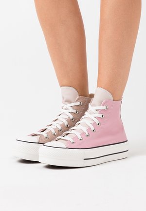 Baskets montantes en cuir rose et beige, lacets blancs, et détails en caoutchouc noir sur la semelle. Bout renforcé texturé et accents cousus.