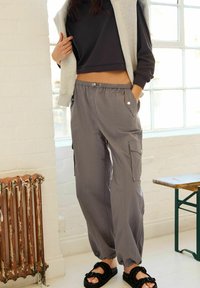 Grå cargo bukser med elastisk talje, sidelommer og løs pasform. Sammen med en cropped sort top og sorte sandaler.