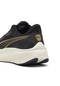 Schwarzer Sportschuh mit goldenen Akzenten, der ein elegantes Design, eine texturierte Oberseite, eine dicke weiße Zwischensohle und eine gemusterte schwarze Außensohle aufweist.