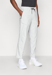 Ανοιχτό γκρι cargo παντελόνι με ελαστική μέση, κορδόνι και πολλές τσέπες. Φτιαγμένο από απαλό ύφασμα, με καμπυλωτό σχέδιο ποδιών και μανίκια στους αστραγάλους.
