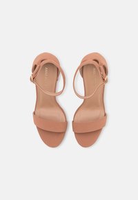 Sandálias de salto de cor pêssego com uma faixa frontal larga, uma faixa delgada no tornozelo e uma fivela em tom dourado. Material sintético suave com um design minimalista.