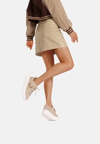 Gonna mini in pelle beige abbinata a sneaker beige chiaro con lacci, caratterizzate da una suola bianca e un sottile accento metallico.