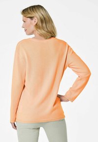 Hellorange Pullover mit langen Ärmeln und rundem Halsausschnitt, bietet eine lockere Passform und Rippdetails am Saum.