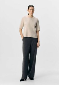 Beige ribbet strikbluse med korte ærmer, parret med grå brede bukser og sorte spidse sko, der har rene linjer og en afslappet pasform.