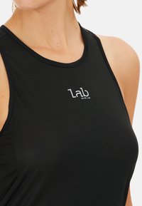 Top sportivo nero senza maniche in tessuto rigato, con scollatura rotonda e un logo bianco che recita "Elite Lab" sul davanti.