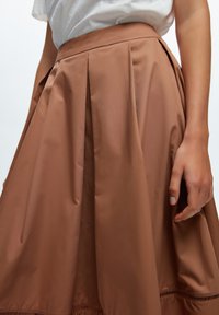 Jupe plissée marron en tissu lisse, avec une taille ajustée et un ourlet doté d'un subtil détail de couture.